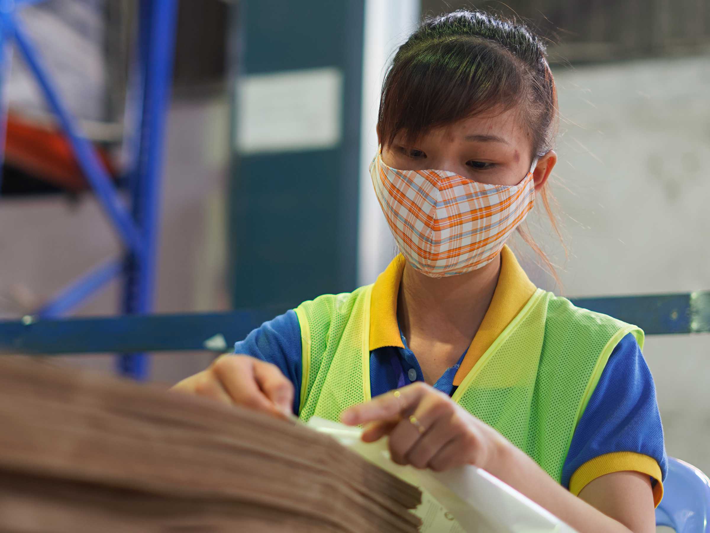 A woman wearing a mask and a safety vest is working in a factory.
